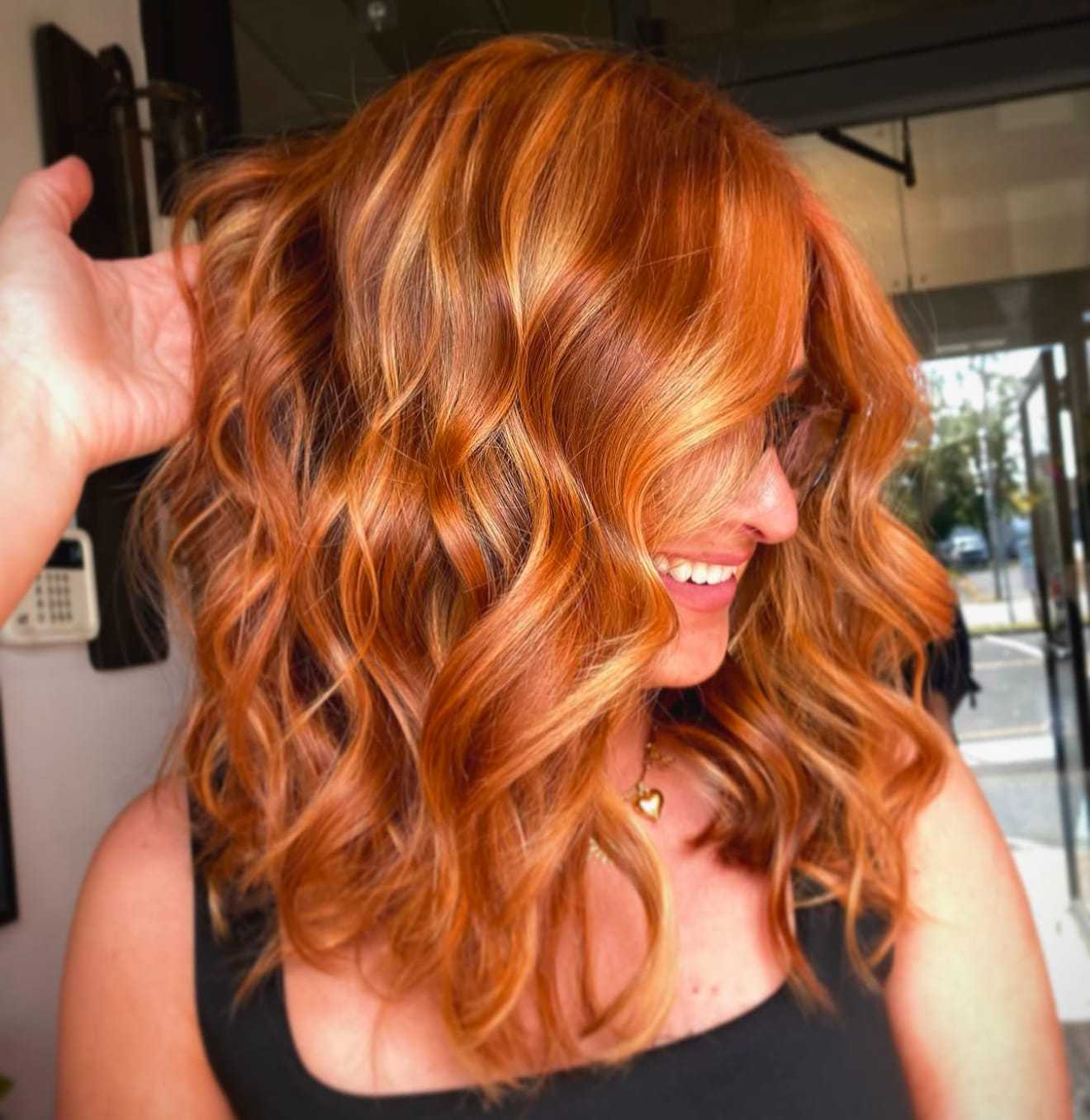 Red hair with soft curls styled in a salon, woman smiling in profile.